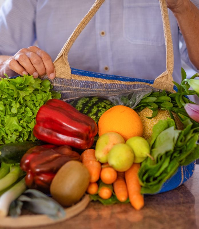 Mature woman from the grocery store places her shopping bag full of vegetables and fruit on the table,healthy eating concept