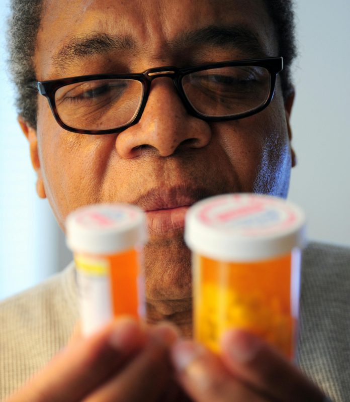 Senior adult man carefully examines two prescription pill bottles indoors.